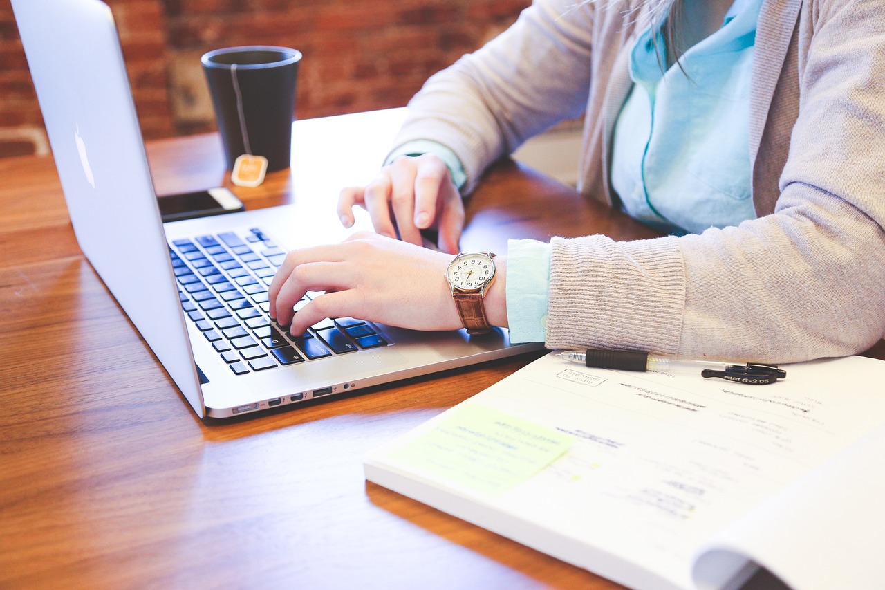 A person at a laptop computer with an open book and cup of tea